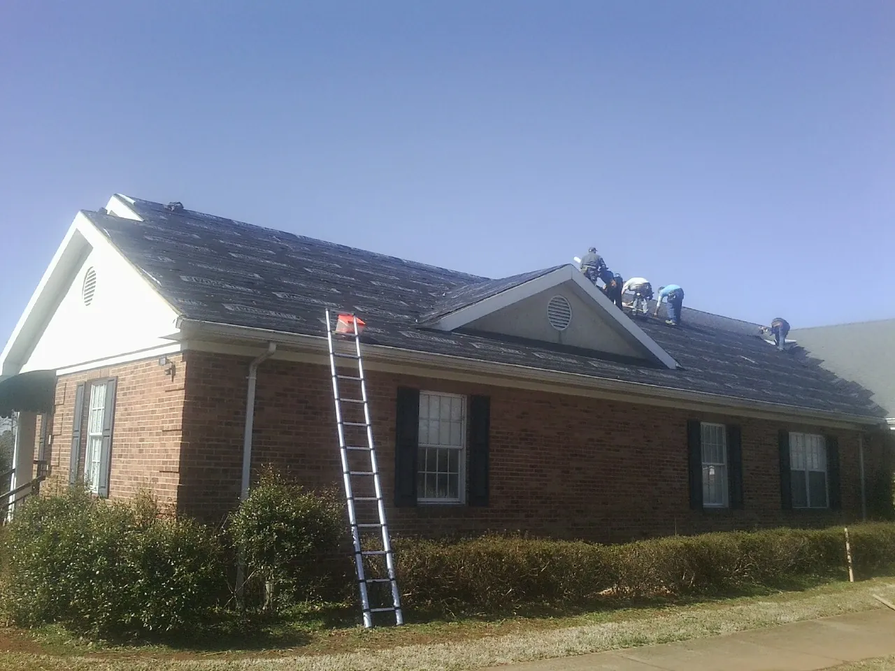 Crew tearing shingles off a brick ranch roof with a ladder set — Emergency Roof Repair work by our crew in Richmond Dale