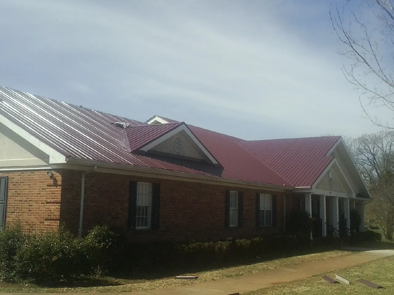 Red metal roof with gabled entries on a long brick building, from a Hail Damage Roof Repair job in Richmond Dale