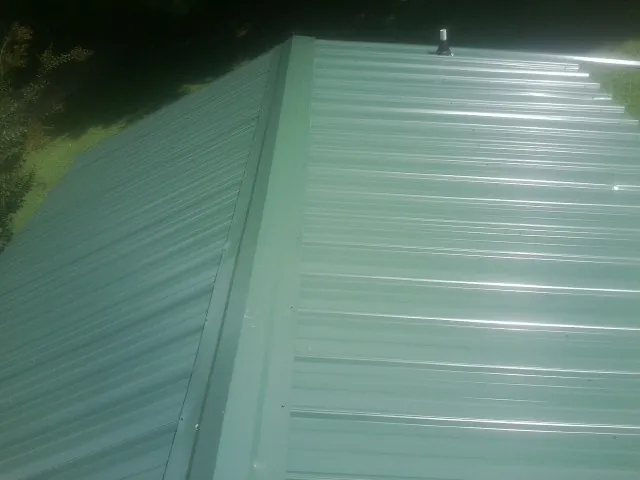 New green metal panels meeting at the ridge of a roof — Flat Roof Repair work by our crew in Richmond Dale