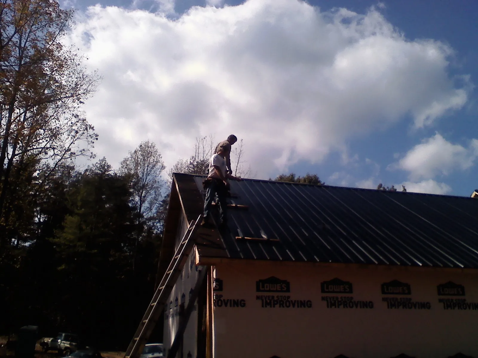 Roofer fastening dark metal panels high against a cloudy sky, from a Roof Inspection job in Richmond Dale