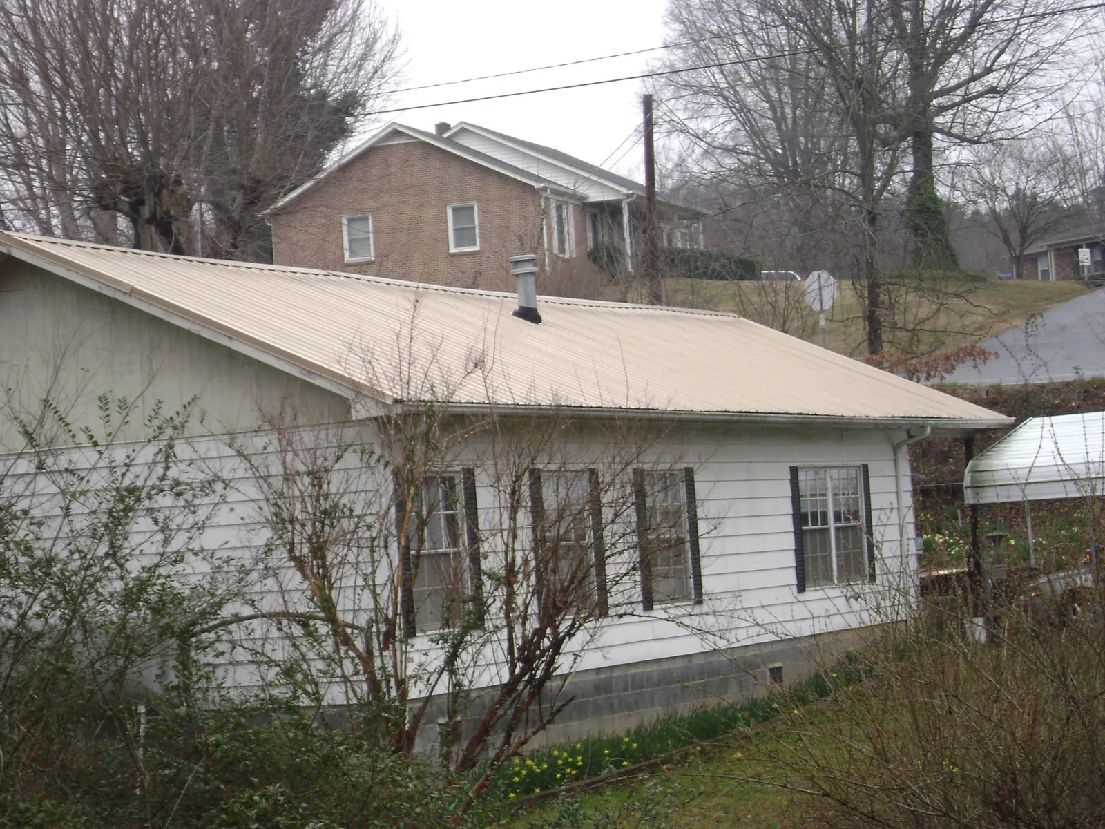 Tan metal roof on a white sided house set into a hillside — Commercial Roofing by Roofing Brothers in Richmond Dale